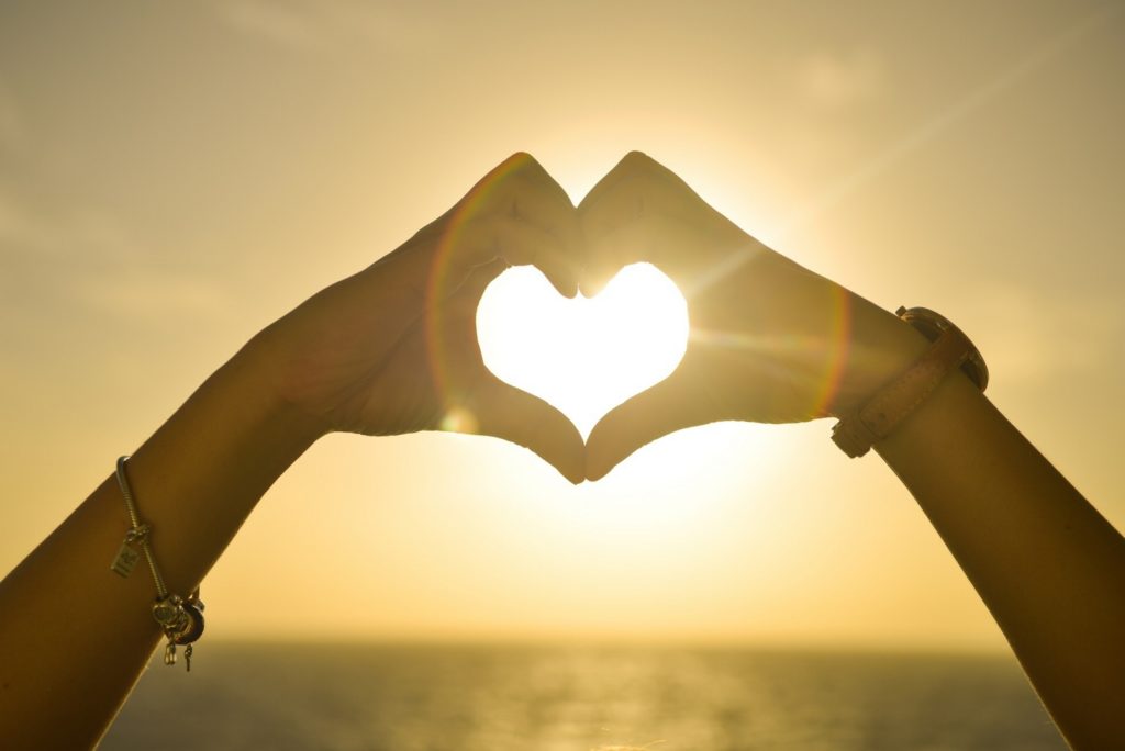 Friends hands together forming a heart in front of sunlight.