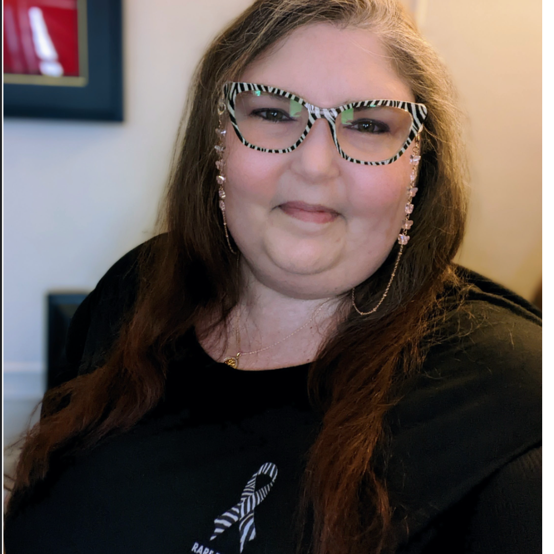 Photo of advocate Kerry Wong wearing zebra print glasses and an awareness ribbon top. Kerry has long light brown hair and is smiling in the photo.